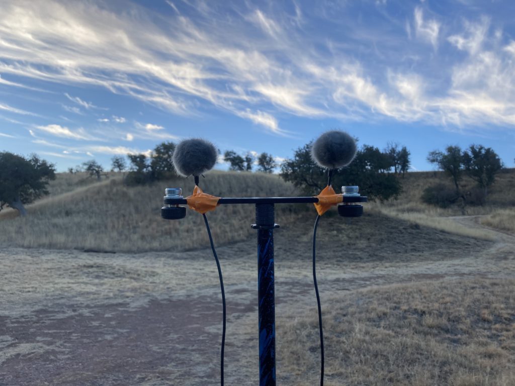 two fuzzy balls spaced about 6 inches apart. They are on top of a T-like mic stand. The fuzzy gray balls have wires trailing down and they are attached to the stand via hastily applied orange masking tape.