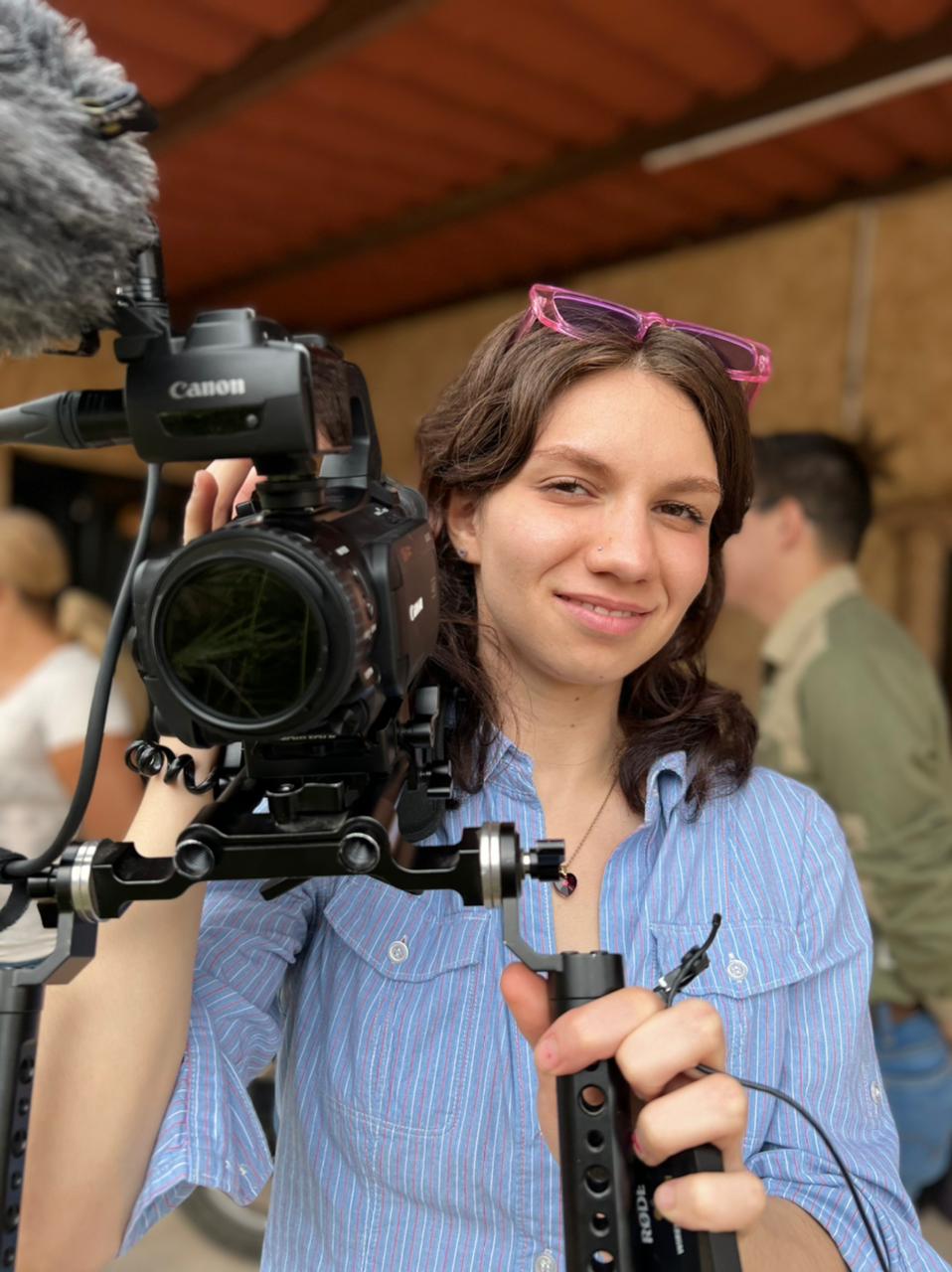 A photograph portrait of a woman holding a video camera pointed at the photographer